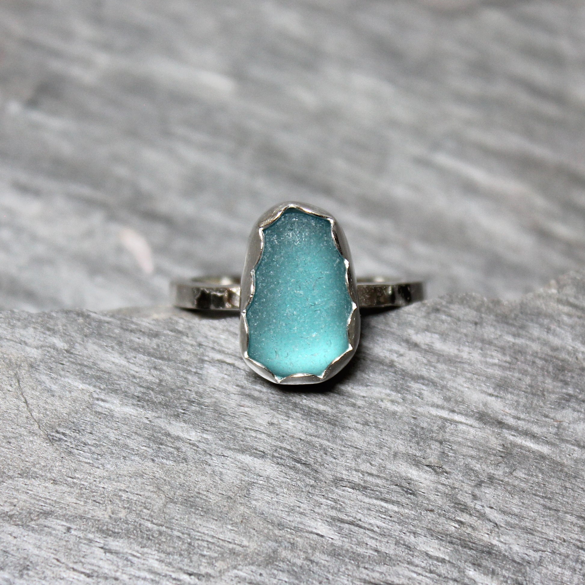 Dark turquoise sea glass ring with silver band on a gray surface