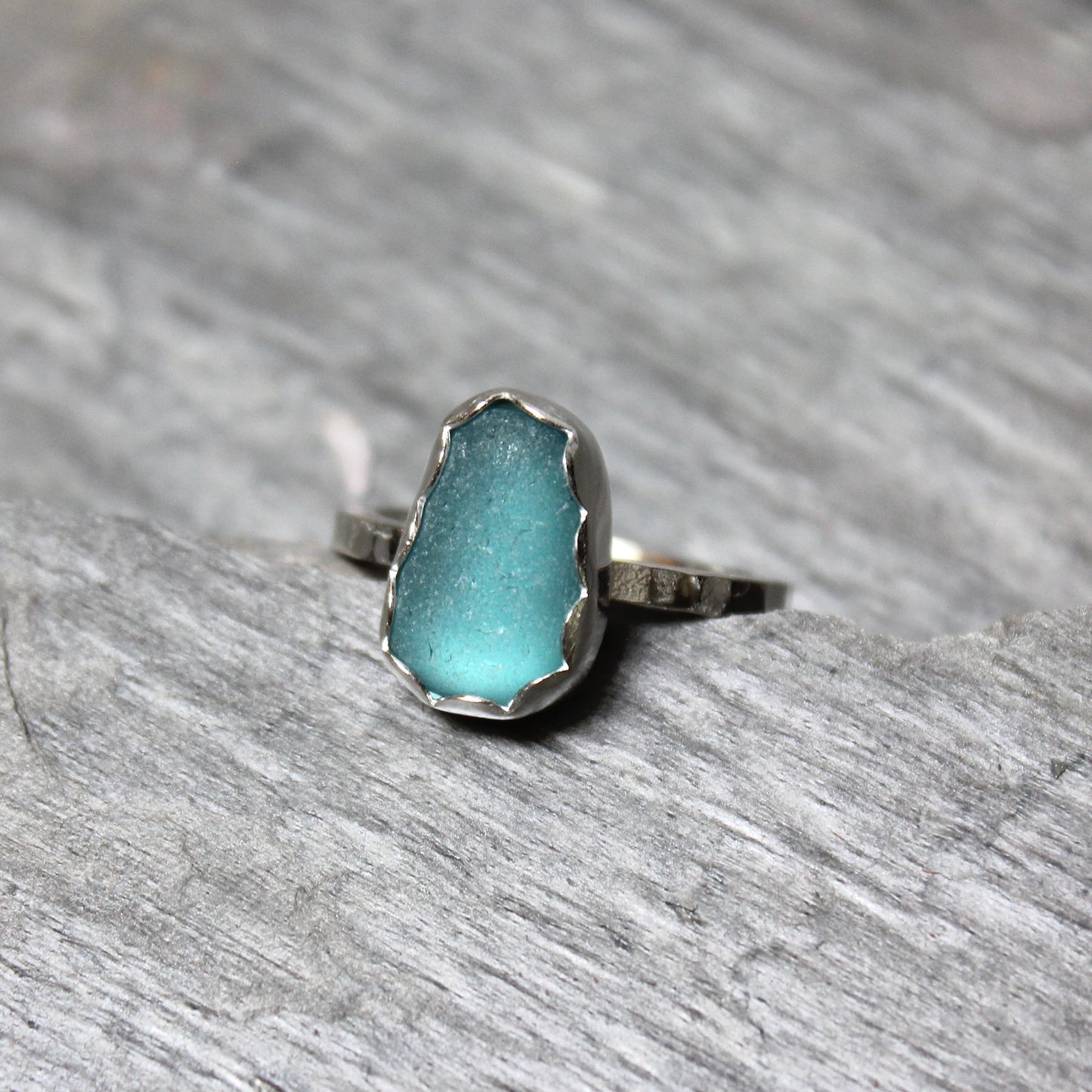Dark turquoise sea glass ring with silver band on a gray surface