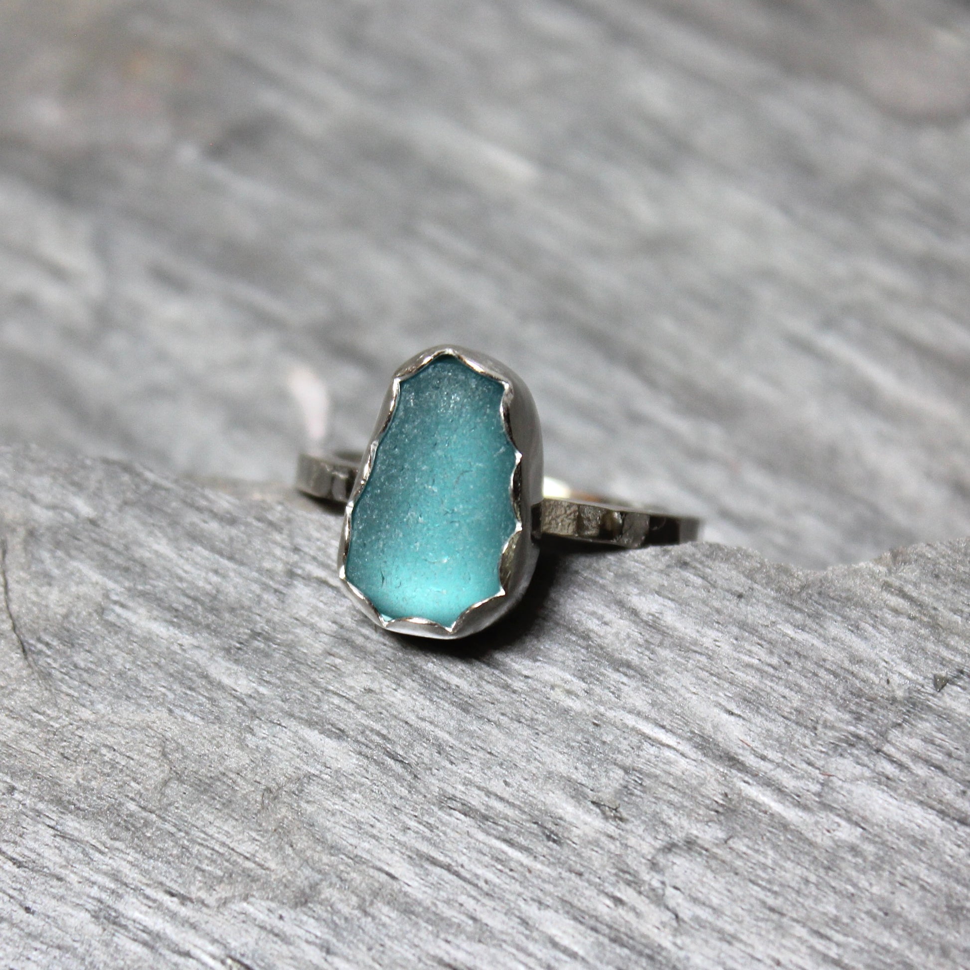 Dark turquoise sea glass ring with silver band on a gray surface
