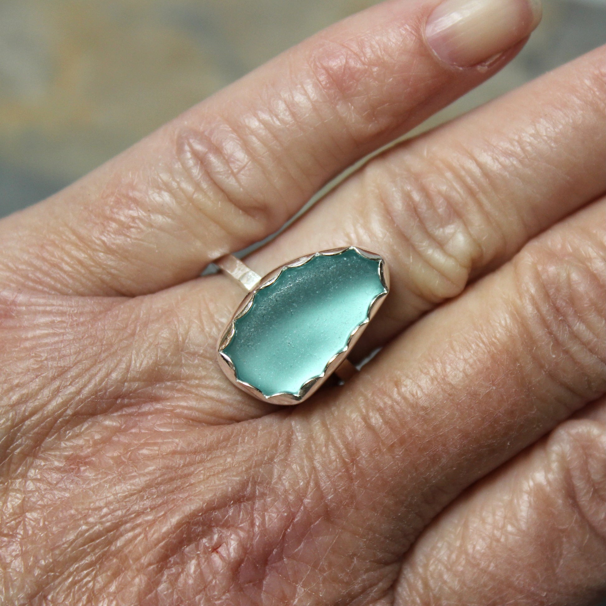 Hand wearing a ring with a turquoise sea glass ring on a blurred background
