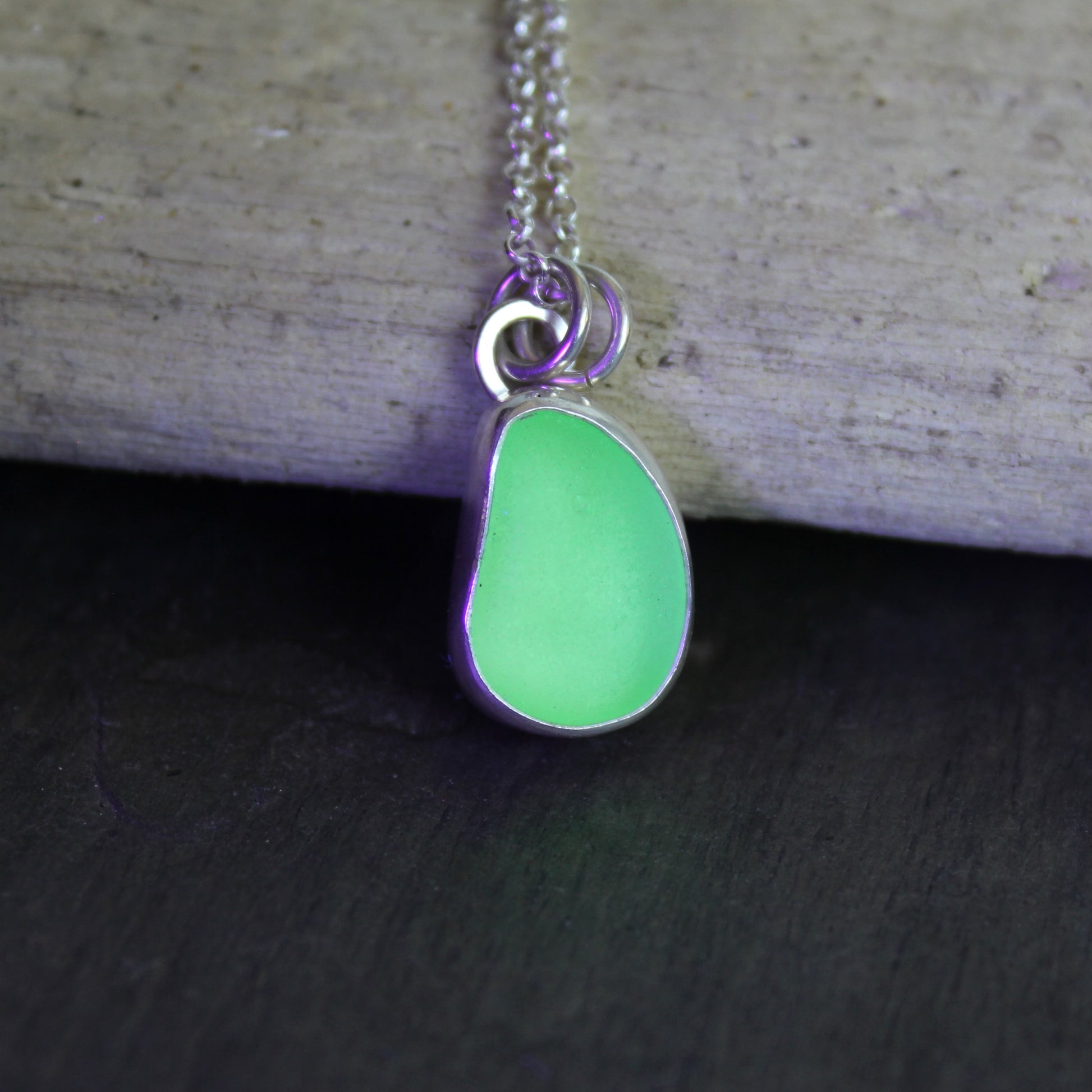 Necklace with a pale-yellow uranium pendant against a clack light on a branch