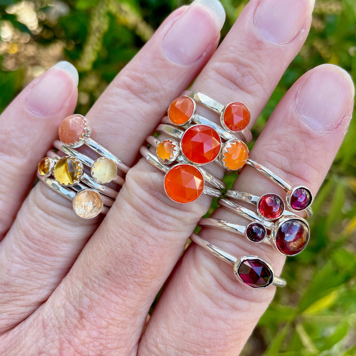 Hand wearing multiple rings with colorful gemstones against a natural background