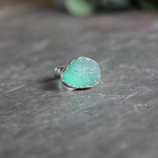 This is a dark teal green piece of sea glass set in a fine and sterling silver scalloped bezel setting on a sturdy silver band.  Size 10
