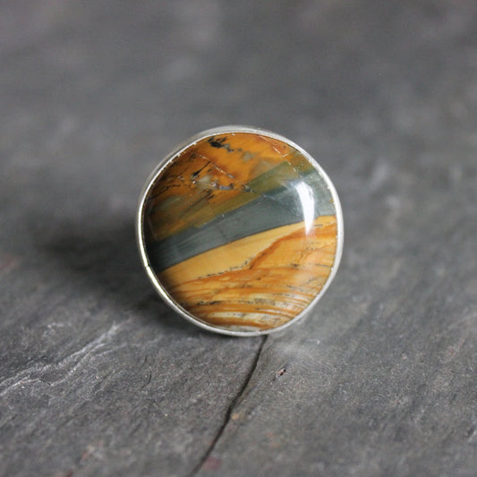 This is a large Owyhee picture jasper set in a fine and sterling silver bezel setting on a sturdy silver band.  The stone has a landscape patter with earth tones and some blue running through it like a river.  Size 8